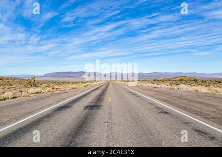 A long road through a remote Nevada landscape, with a blue sky overhead Stock Photo