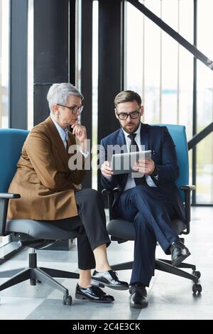 Two business colleagues sitting on chairs and using digital tablet in their work they are at modern office building Stock Photo