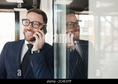 Mature businessman in suit smiling while has a conversation on the phone at office corridor Stock Photo