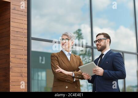 Business colleagues talking to each other while standing outdoors and using digital tablet Stock Photo