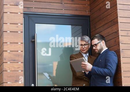 Two business colleagues using digital tablet together while standing outdoors near the office door Stock Photo