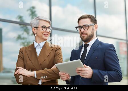 Mature business couple talking and using digital tablet while walking outdoors in the city Stock Photo
