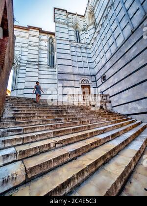 Caucasian female tourist descending marble steps outside Siena Cathedral Bapistery. Italy. Stock Photo