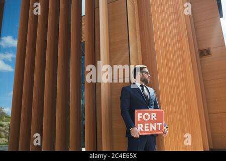 Mature businessman in suit holding placard while standing against the office building he working outdoors Stock Photo