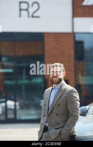 Portrait of young bearded man in eyeglasses smiling at camera while standing in the city Stock Photo