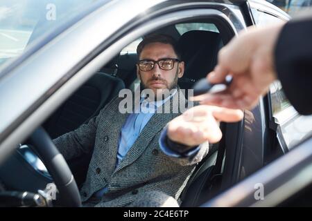 Mature businessman renting the car for business trip he getting keys from manager while sitting in car salon Stock Photo