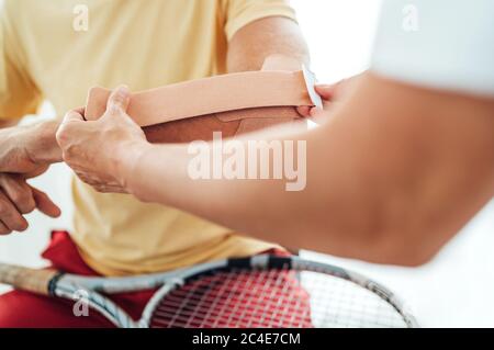 Tennis player elbow taped with elastic therapeutic or Kinesio tape applied by nurse at orthopedic ward close up image. Active sporty people health reh Stock Photo
