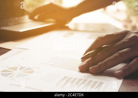 Young businessman holding pen on charts and graph to find out the result at home office. Stock Photo