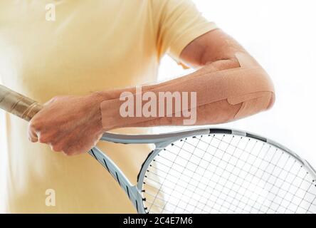 Tennis player elbow taped with elastic therapeutic or Kinesio tape applied on arm lying on racket at orthopedic ward close up image. Active sporty peo Stock Photo