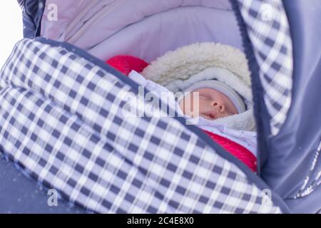 A little newborn baby sleeps on a walk in a pram on a winter day. Stock Photo