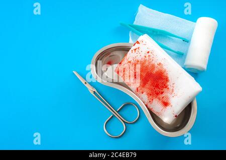 Medical waste, used surgery supplies and first aid concept with roll of gauze bandages, kidney dish, scissors and bloody used bandage covered in blood Stock Photo