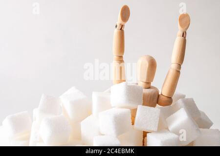Sugar addiction, insulin resistance, unhealthy diet and November 14 is diabetes awareness day concept with a puppet drowning in sugar cubes isolated o Stock Photo