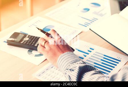 Occupation financial asian young man calculate statistics number on desk home office with pressing button calculator and holding pen for make note on Stock Photo