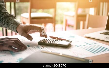 Businessman standing and using calculator about summary report on desk in office room. Stock Photo