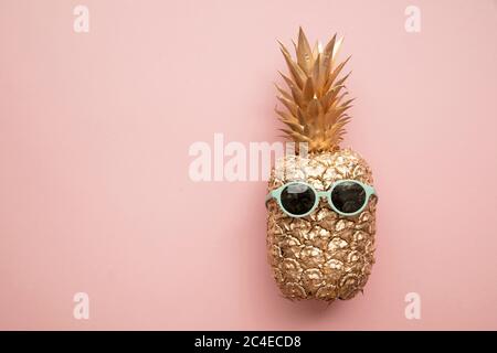Gold trendy pineapple wearing summer sunglasses on pink Stock Photo
