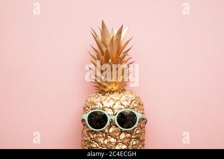 Gold trendy pineapple wearing summer sunglasses on pink Stock Photo