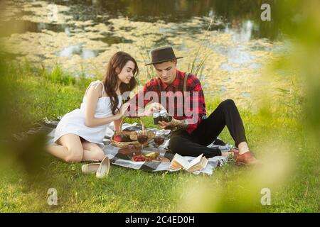 Talking. Caucasian young, happy couple enjoying weekend together in the park on summer day. Look lovely, happy, cheerful. Concept of love, relationship, wellness, lifestyle. Sincere emotions. Stock Photo