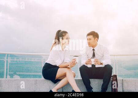 Two asian business people talking outside company with holding coffee and break relaxing time concept. Stock Photo