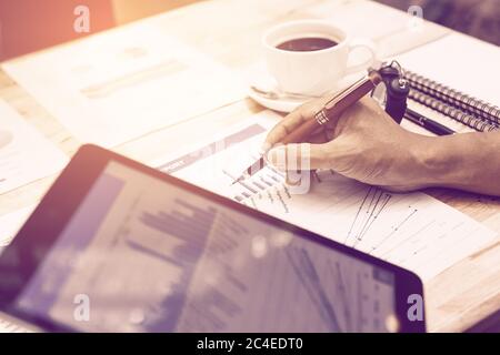 Hand businessman pointing on summary chart report and holding tablet for looking data information. Stock Photo