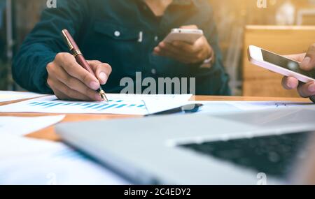 Businessman writing or pointing summary report chart and using smart phone looking data. Stock Photo