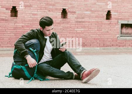 Asian traveler man sitting on the street and using smartphone. Stock Photo