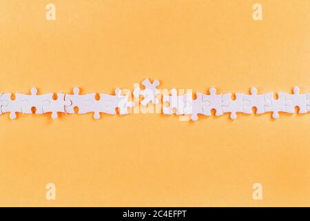 Disrupted row of white jigsaw puzzle pieces with missing link on orange background Stock Photo