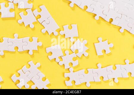 Disassembled white jigsaw puzzle pieces on yellow background. Stock Photo