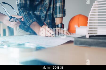 Two casual startup architects are talking about the structure in blueprint paper on table at home office. Stock Photo