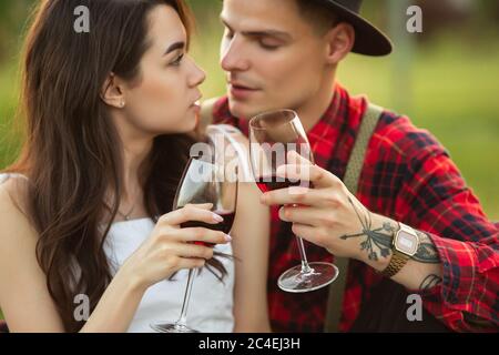 Clinking glasses. Caucasian young couple enjoying weekend together in the park on summer day. Look lovely, happy, cheerful. Concept of love, relationship, wellness, lifestyle. Sincere emotions. Stock Photo