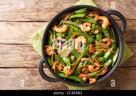 Healthy food of fried shrimp with onions, carrots and pods of snow peas close-up in a plate on the table. horizontal top view from above