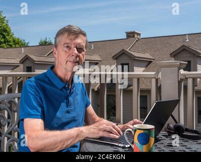 Senior caucasian man working from home during coronavirus epidemic using laptop and smiling at the camera Stock Photo