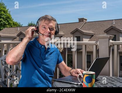 Senior caucasian man working from home during coronavirus epidemic using headset and laptop to communicate Stock Photo