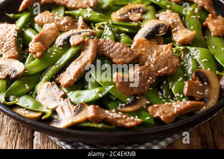 Asian stir-fried beef with mushrooms champignons and pods of green peas, sesame seeds close-up in a plate on the table. horizontal Stock Photo