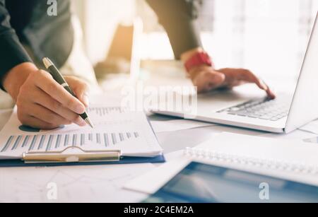 Businessman holding pen and pointing paper chart summary analyzing annual business report with using laptop at room office desk. Stock Photo