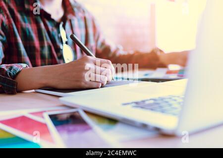 Freelance creative designers working on desk using digital graphic tablet and drawing with pen in modern home office. Stock Photo
