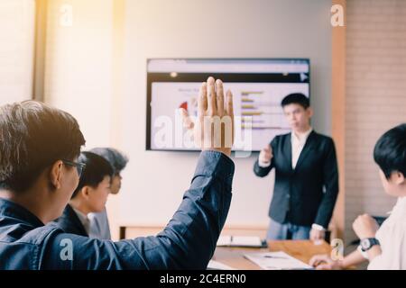 Rear view of a businessman raising hand wants to ask something in boardroom. Stock Photo