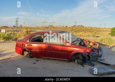 Victorville, CA / USA – May 22, 2020: A red abandoned four door sedan with missing engine and tires in Victorville, California. Stock Photo