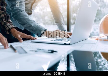 Two architect people working on laptop and checking blueprints in office. Stock Photo