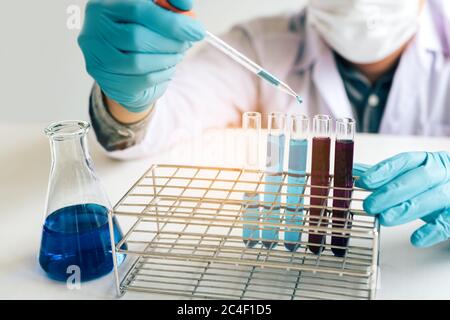Science doing experiment in laboratory adding liquid in test tube with working on assignment in lab. Stock Photo