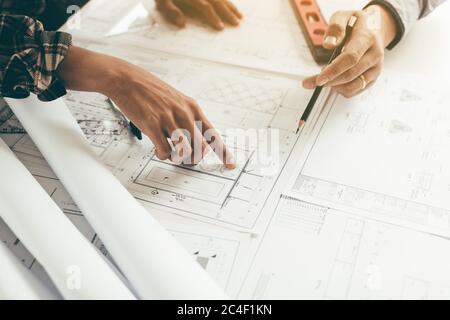 Close up two architect hands holding pencil and pointing on building blueprints in office room. Stock Photo