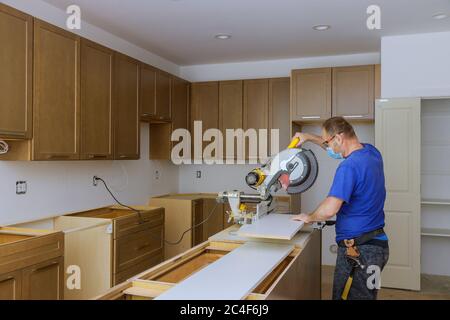 Worker protects himself from covid-19, man cut using circular saw rotating saw cutting wooden installation of in the kitchen of installation cabinets remodel Stock Photo