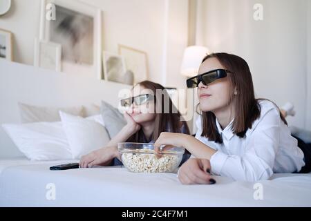 Happy friends or teenage girls with 3D glasses eating popcorn and watching movie at home Stock Photo