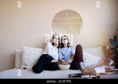Frightened friends or teenage girls with 3D glasses eating popcorn and watching movie at home Stock Photo