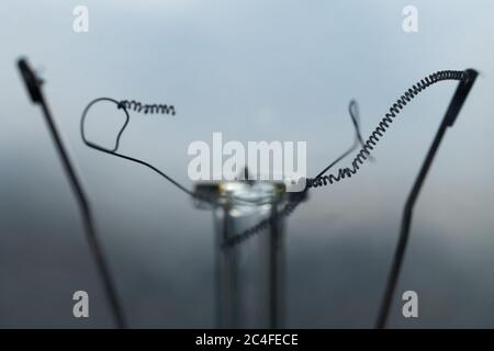 Macro photo of a broken wire filament of a burned incandescent light bulb. Non-functional electric light bulb. Burnt lightbulb. Fired-on lamp. Stock Photo
