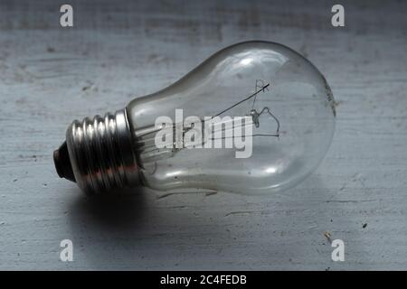 Burned out old light bulb lying on the wooden painted white surface Stock Photo