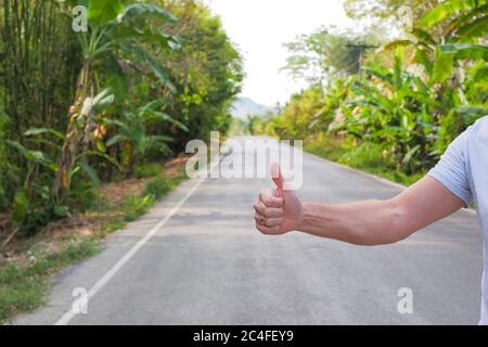 Travel, trip, vacation, wanderlust. Hitchhiker sign on road. Thumbs up male hand gesture outdoors. Hitchhiking, hitching, thumbing, auto stop concept