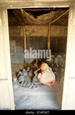 A woman works on earthen pots and vases. Colourful earthenware like pots, jars, and vases enhance the beauty of city households. Besides, it is a sour Stock Photo