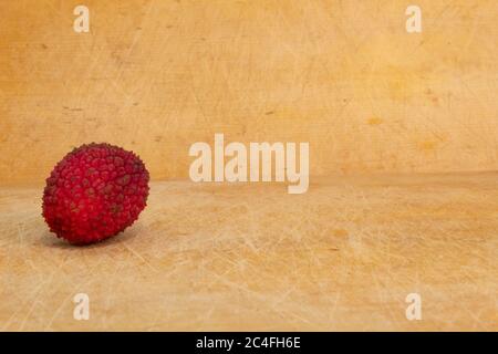 one single red lychee on a wooden colored background Stock Photo