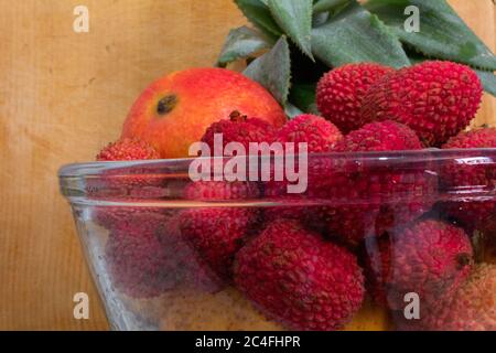 close up of a glass bowl with many tropical fruits like pineapples, mangoes and lychees, on a wooden background Stock Photo