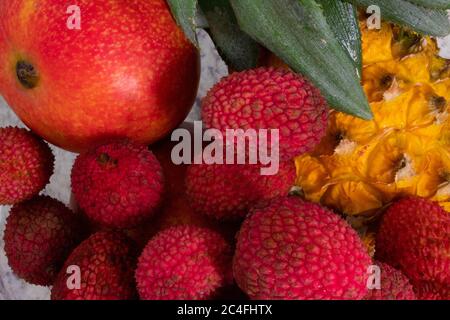 close up of a glass bowl with many tropical fruits like pineapples, mangoes and lychees, on a light colored background Stock Photo